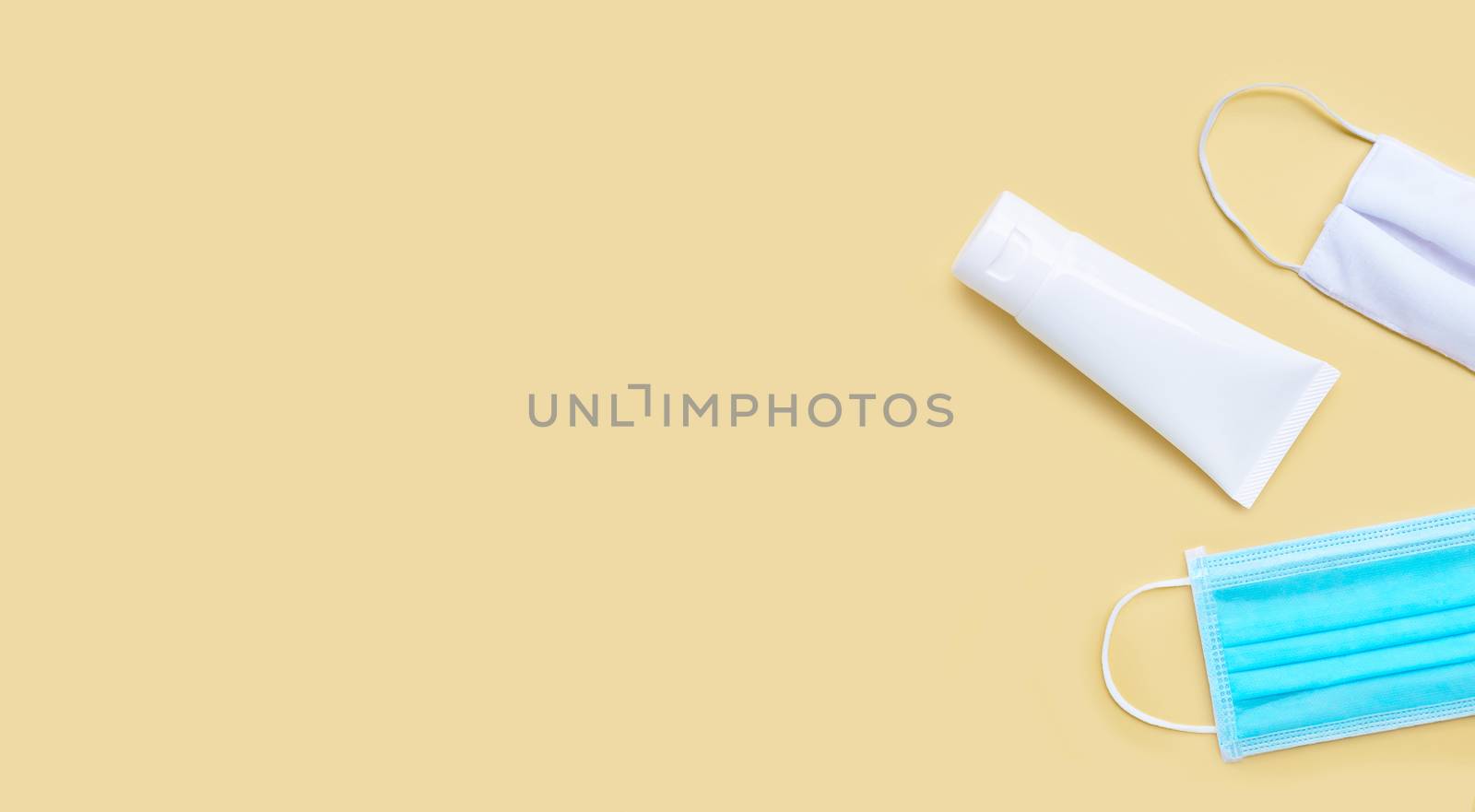 Masks and Alcohol hand sanitizer gel in white glossy plastic tube for hygiene corona virus (Covid-19) protection. Yellow background with copy space