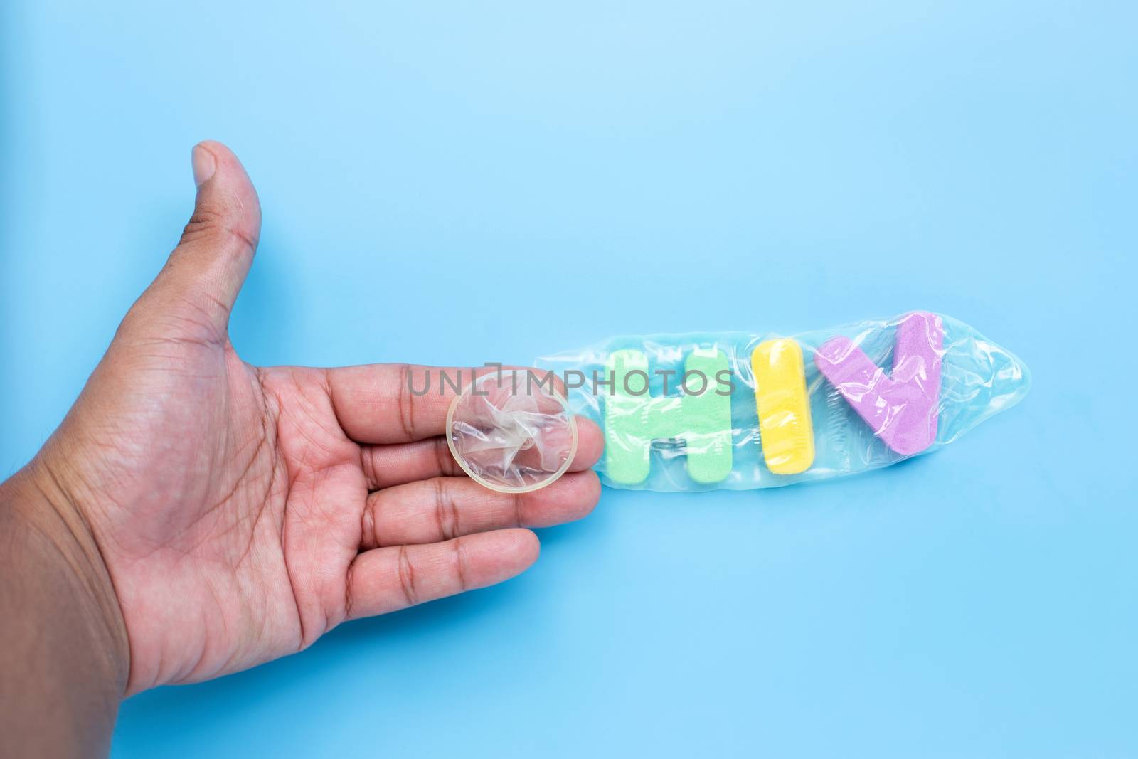 Hand with  "HIV" colorful alphabet in condom on blue background. Save sex concept, Topv view