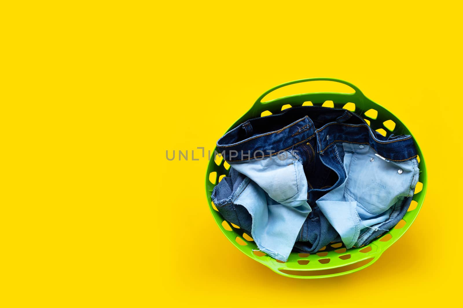 Jeans in green laundry basket on yellow background. Copy space