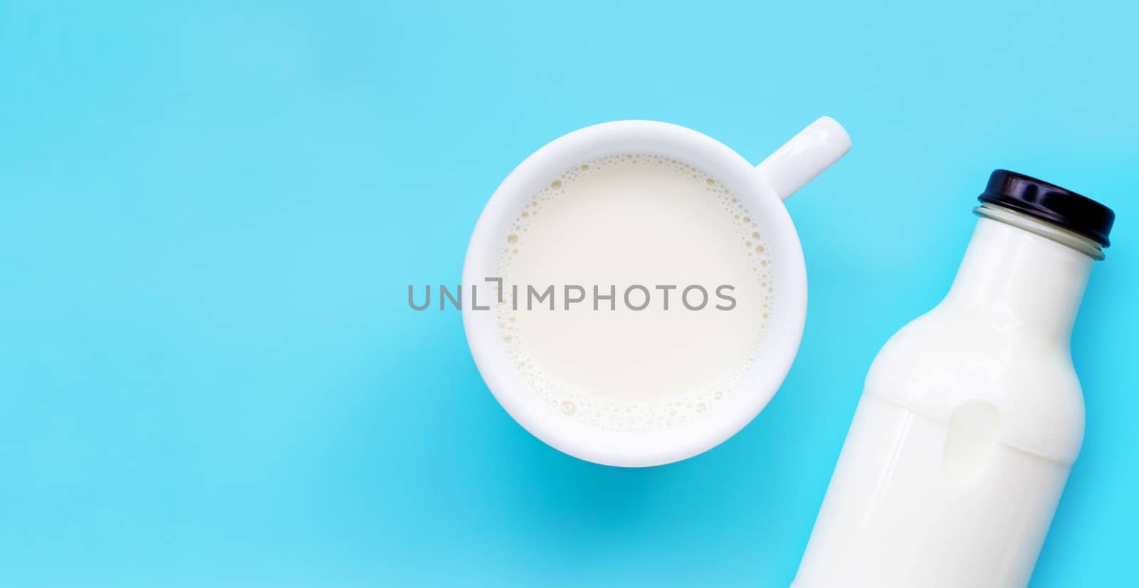Cup of milk and bottle on blue background. Copy space