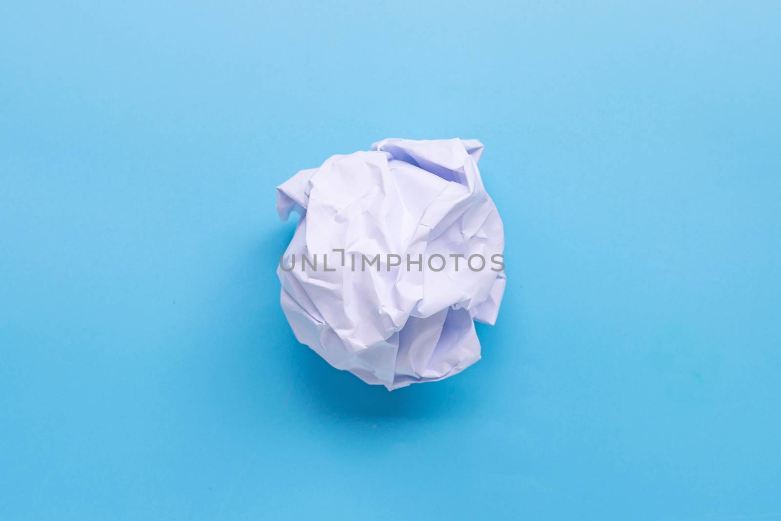 Crumpled paper ball on blue background. Top view