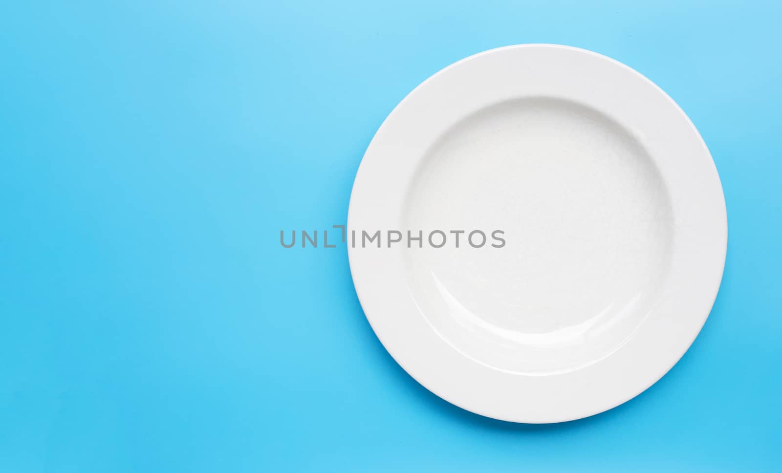 Empty white ceramic plate on blue background. Copy space