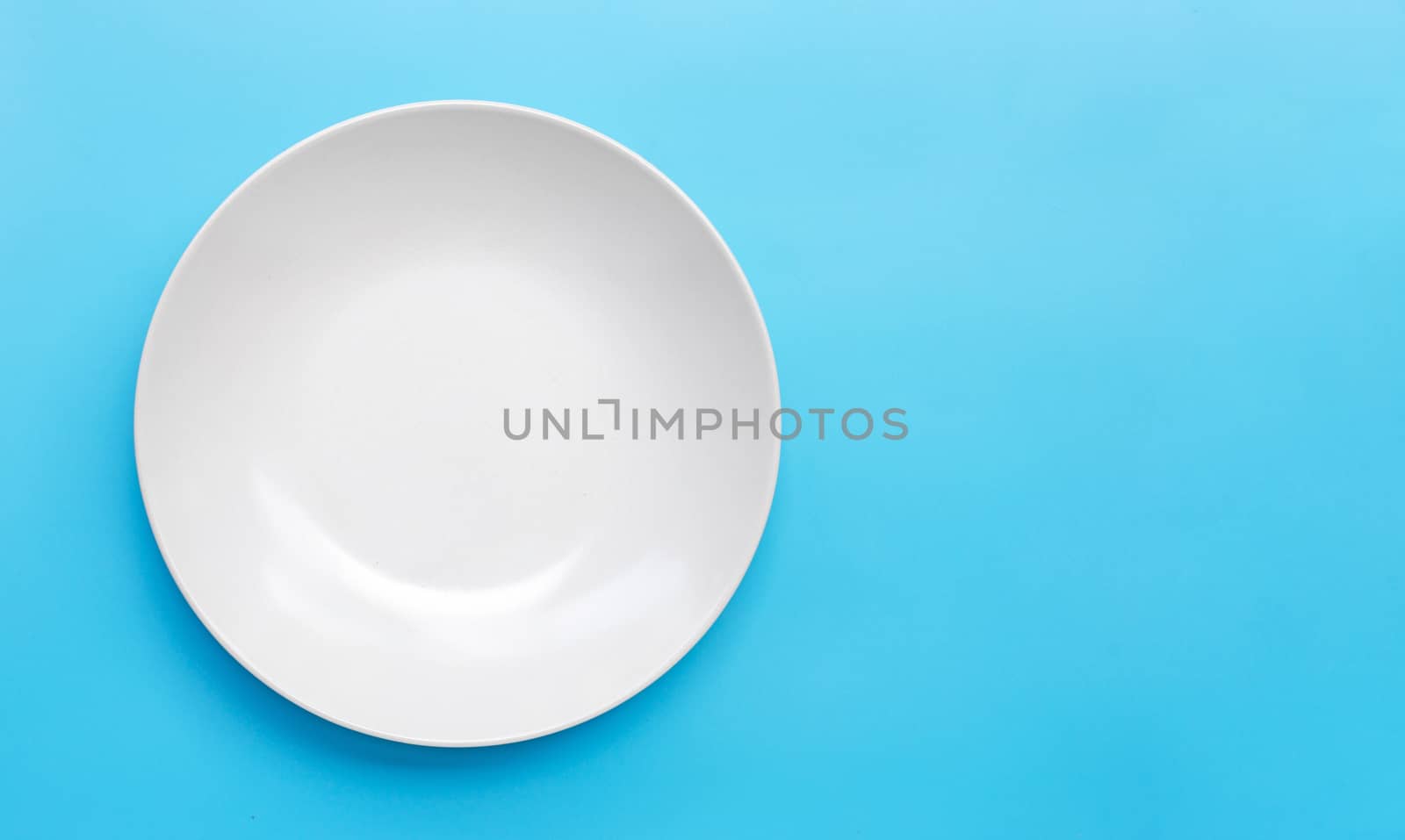 Empty white ceramic plate on blue background. Copy space