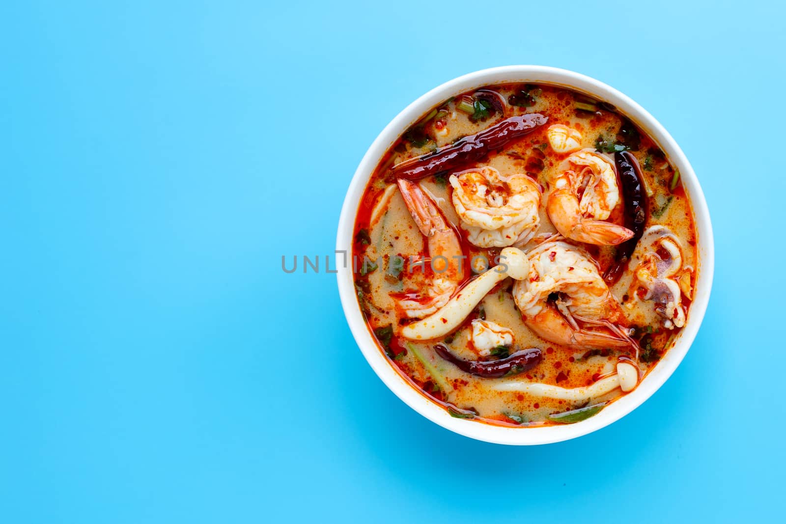  Thai cuisine "Tom Yam Kung" in white bowl. Hot and spicy soup on blue background. Copy space