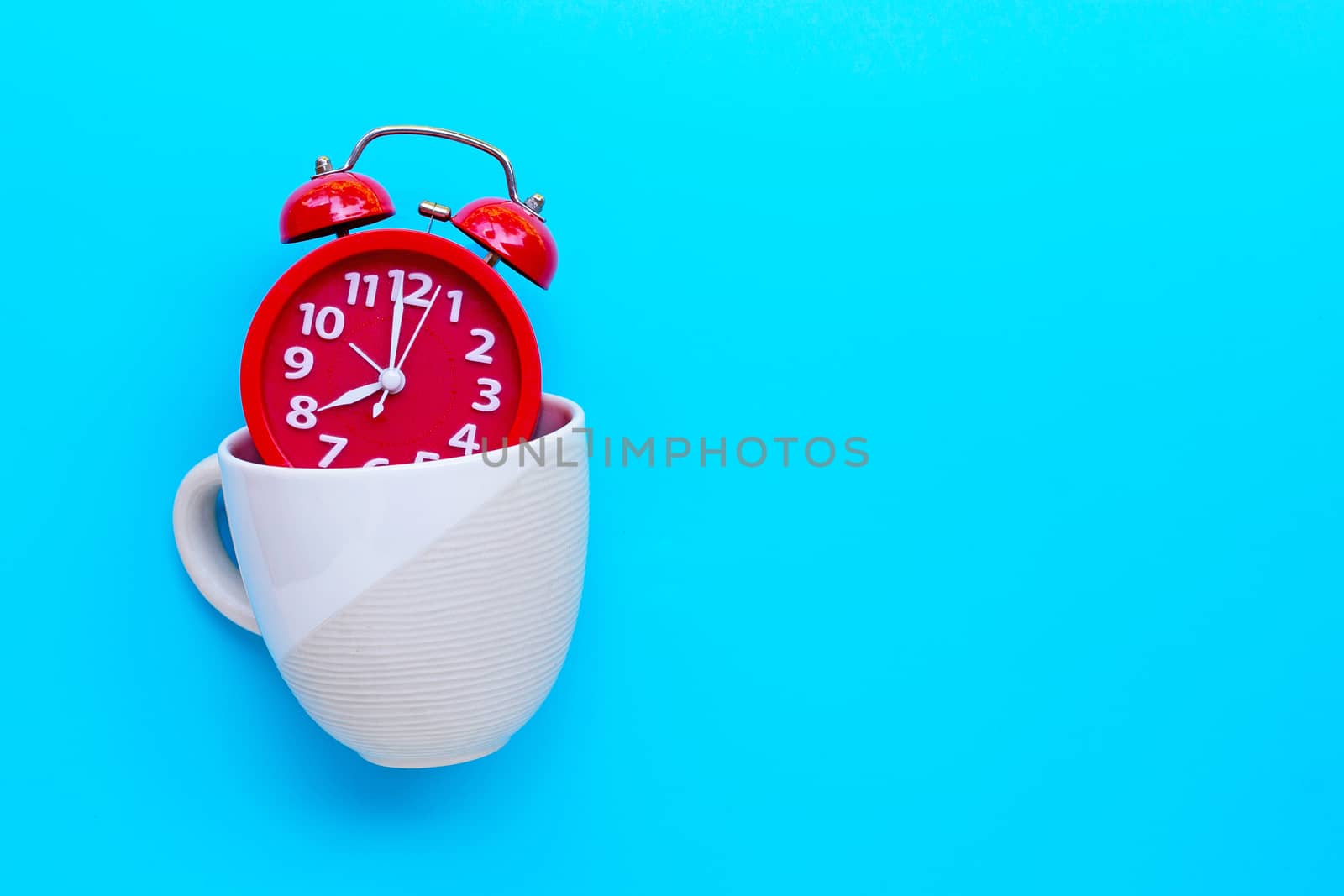 Red alarm clock in coffee cup on blue background. Copy space