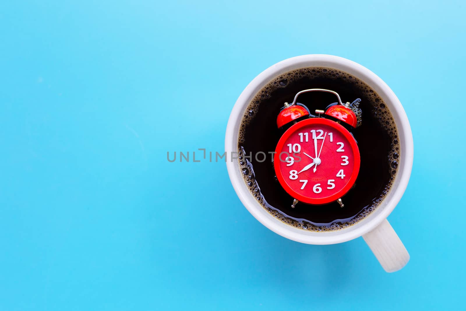 Red alarm clock in coffee cup on blue background. Copy space
