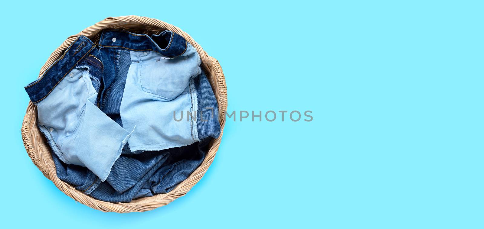 Jeans in laundry basket on blue background. Top view