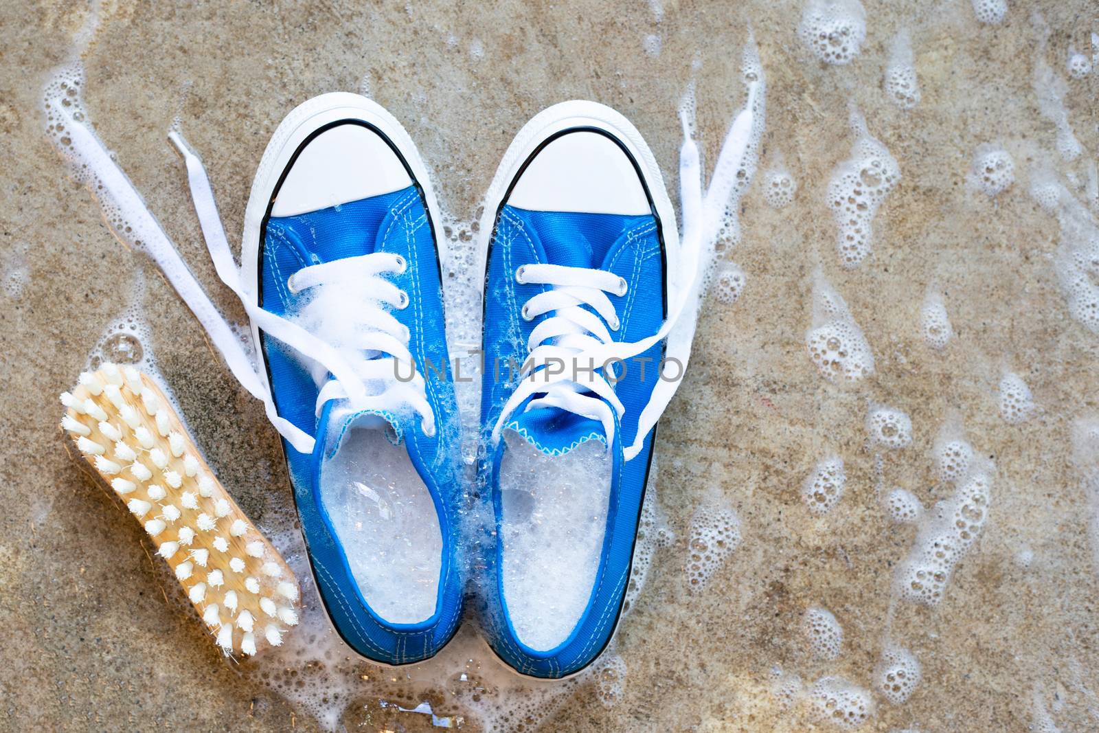 Sneakers with foam of powder detergent water dissolution and wooden brush on cement floor. Washing dirty shoes. Top view
