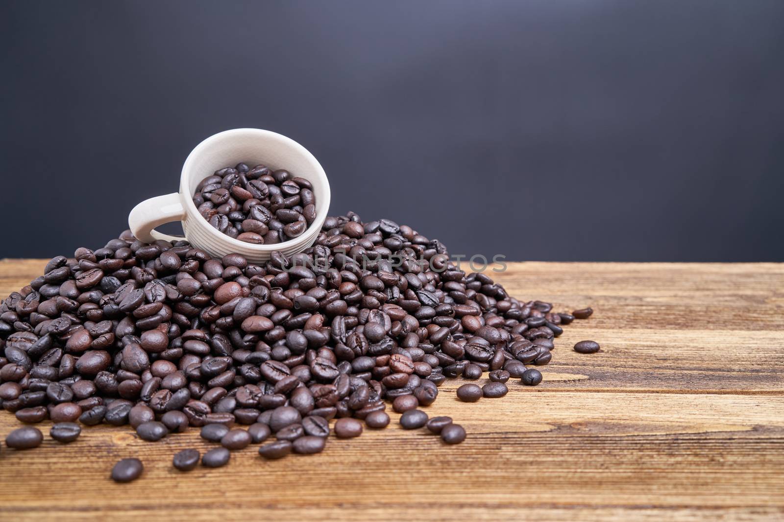 Close up coffee bean in white cup place on pile of coffee bean overflow on old wooden table with black background and copy space.