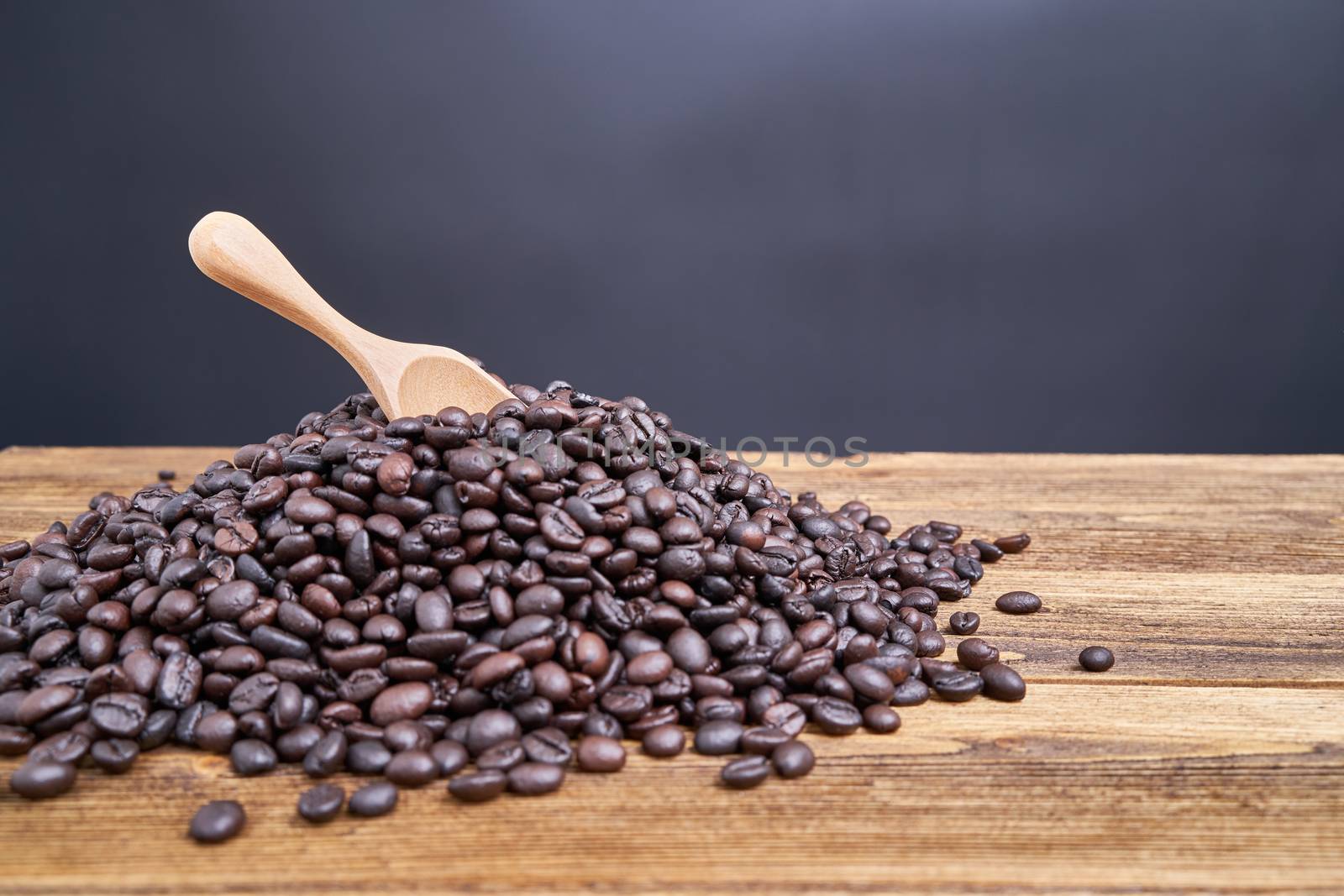 Close up wood spoon put on pile of coffee bean overflow on old wooden table with black background and copy space.