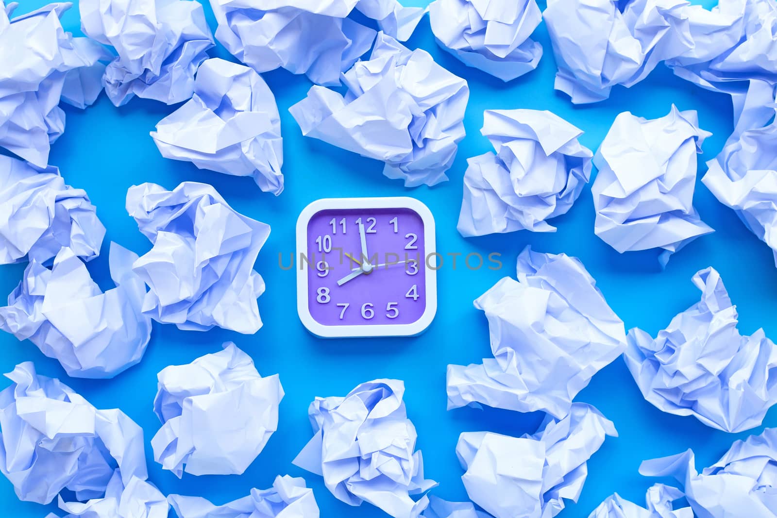 Square clock with white crumpled paper balls on a blue background. Top view