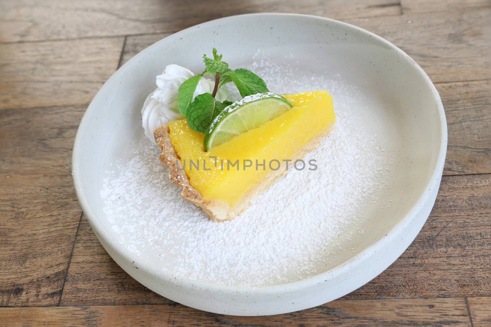 A slice of lemon pie with whipped cream on a white ceramic plate. Wooden background.