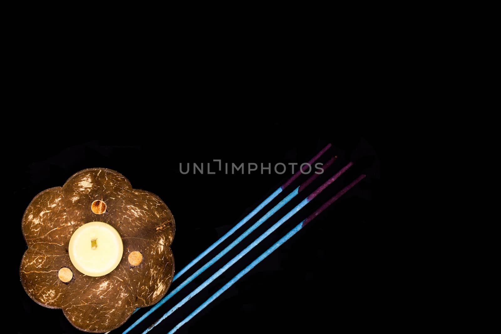 a scented candle on a coconut shell and some blue incense sticks on dark background, oriental simplicity concept