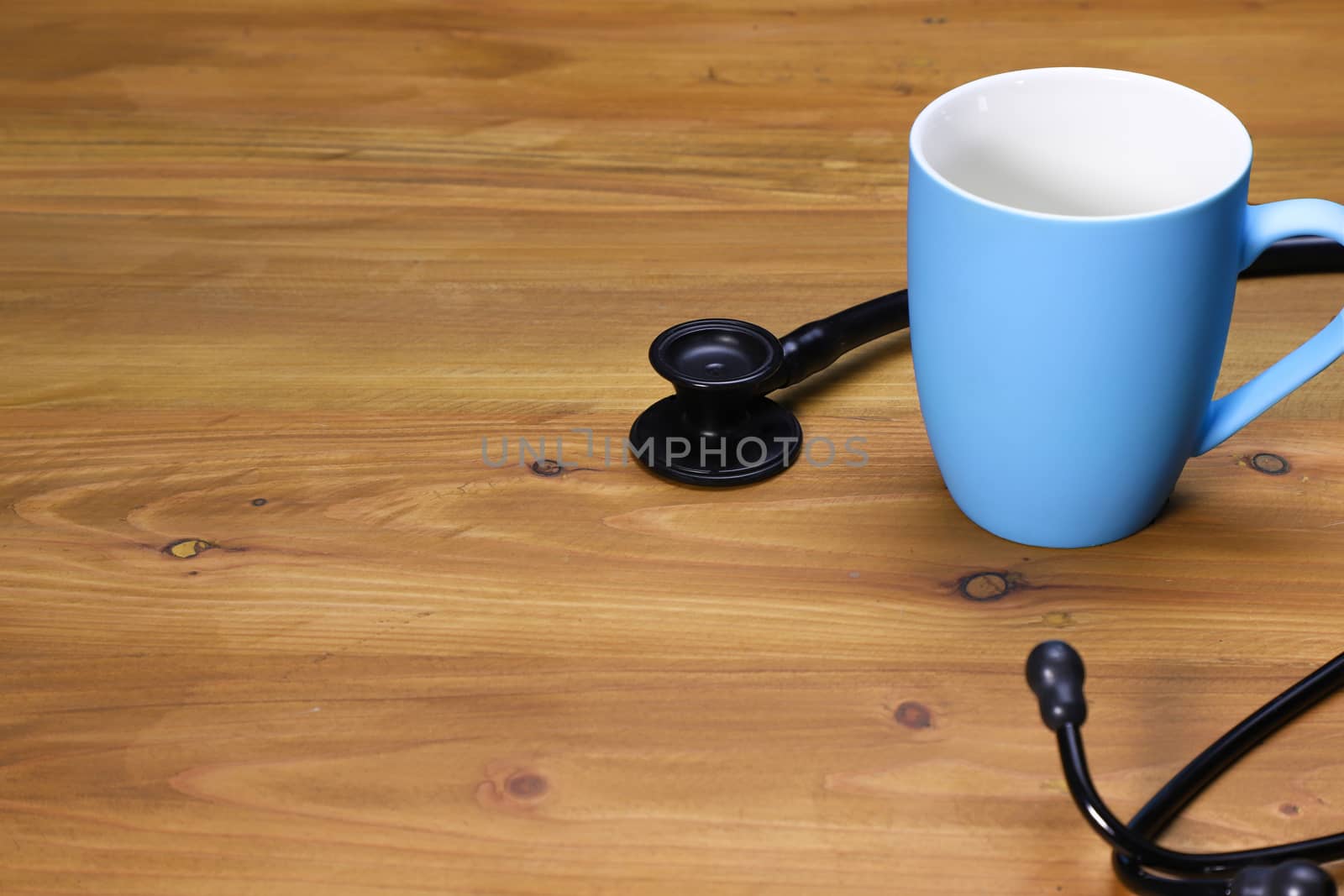 a black stethoscope and a blue ceramic coffee mug on a brown wooden table