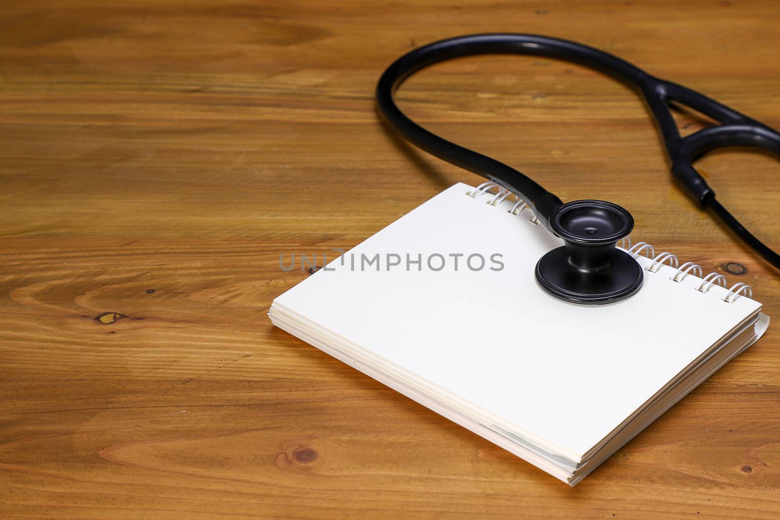 a black stethoscope and a white spiral notebook on a brown wooden table