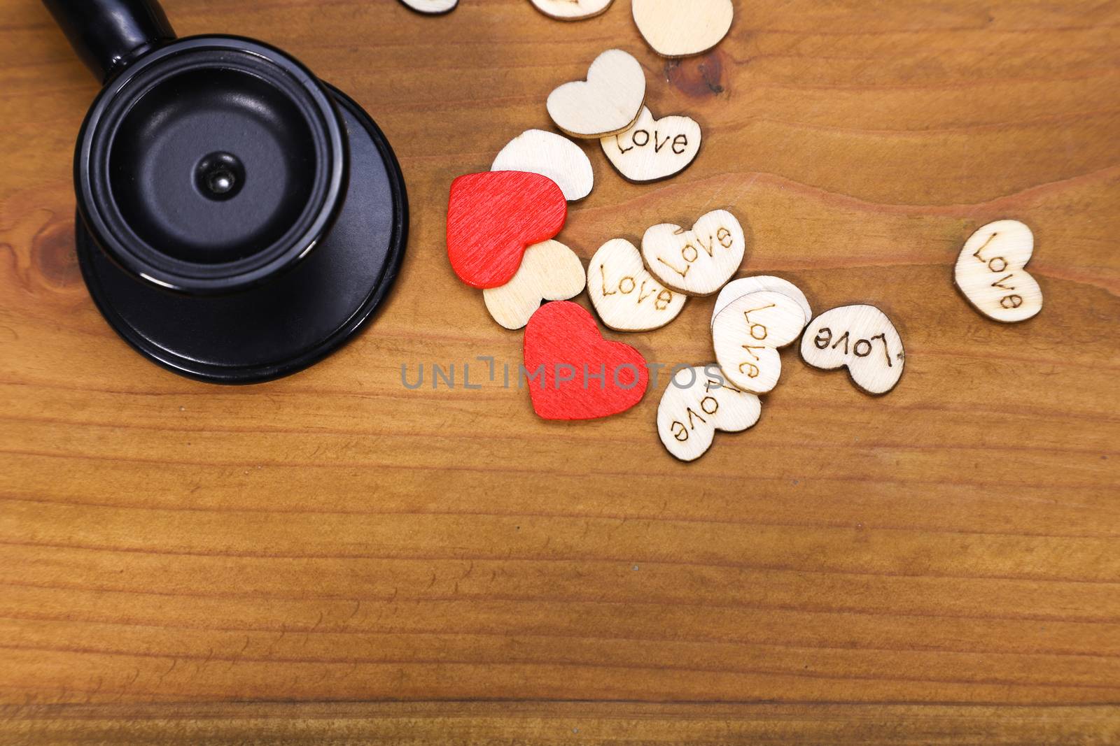 A black stethoscope and a few heart-shaped wooden pieces on wooden top blackground, top view, macro