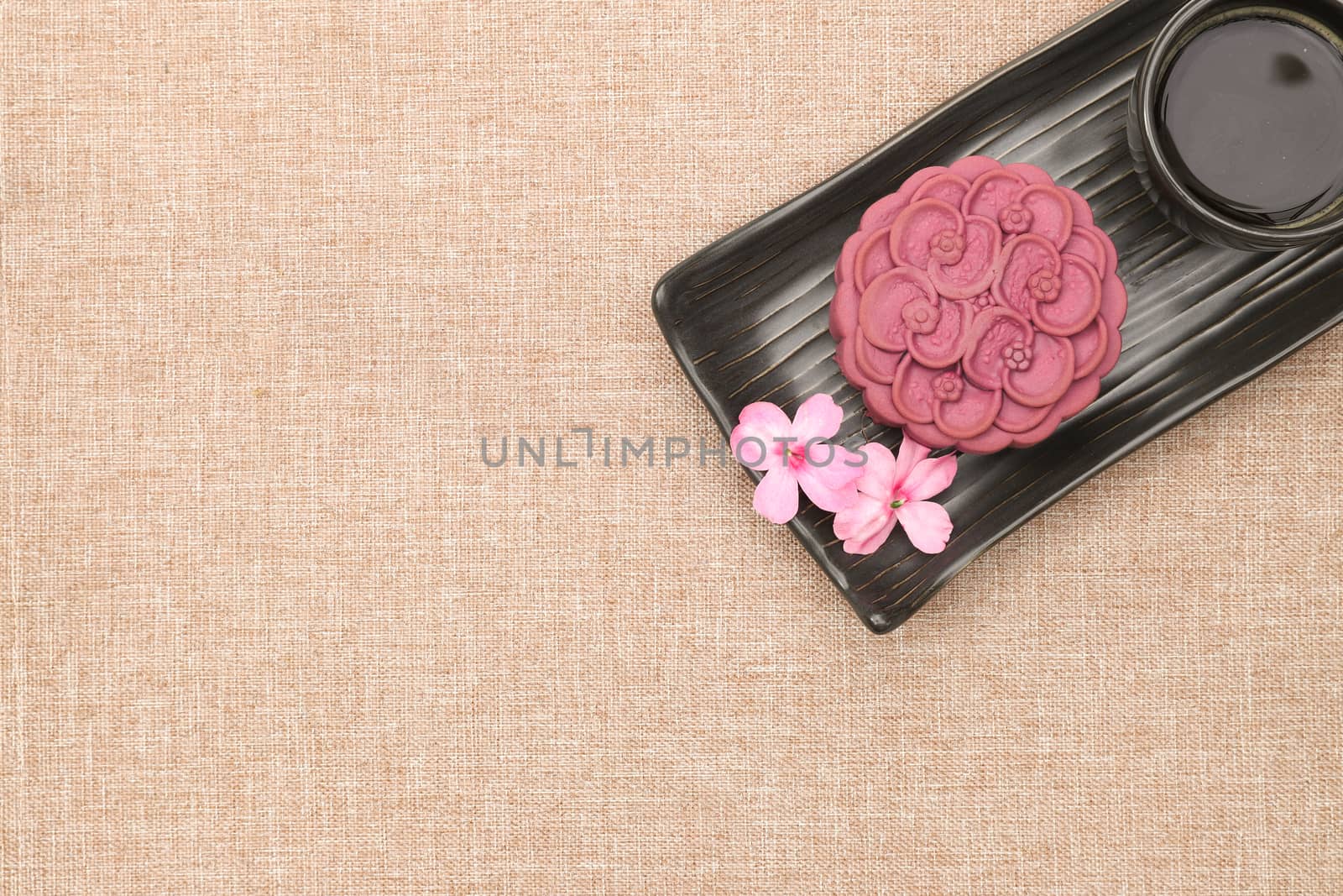 A non-traditional chinese moon cake made of purple japanese yam on a black ceramic plate with a cup of espresso. Top view, light brown linen background.