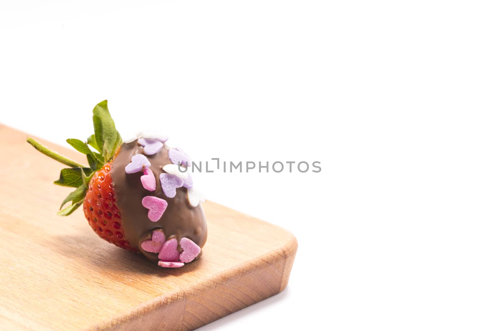 a chocolate coated strawberry with small heart-shape sugar confetti, on a brown wooden cutting board isolated on white background, Valentine