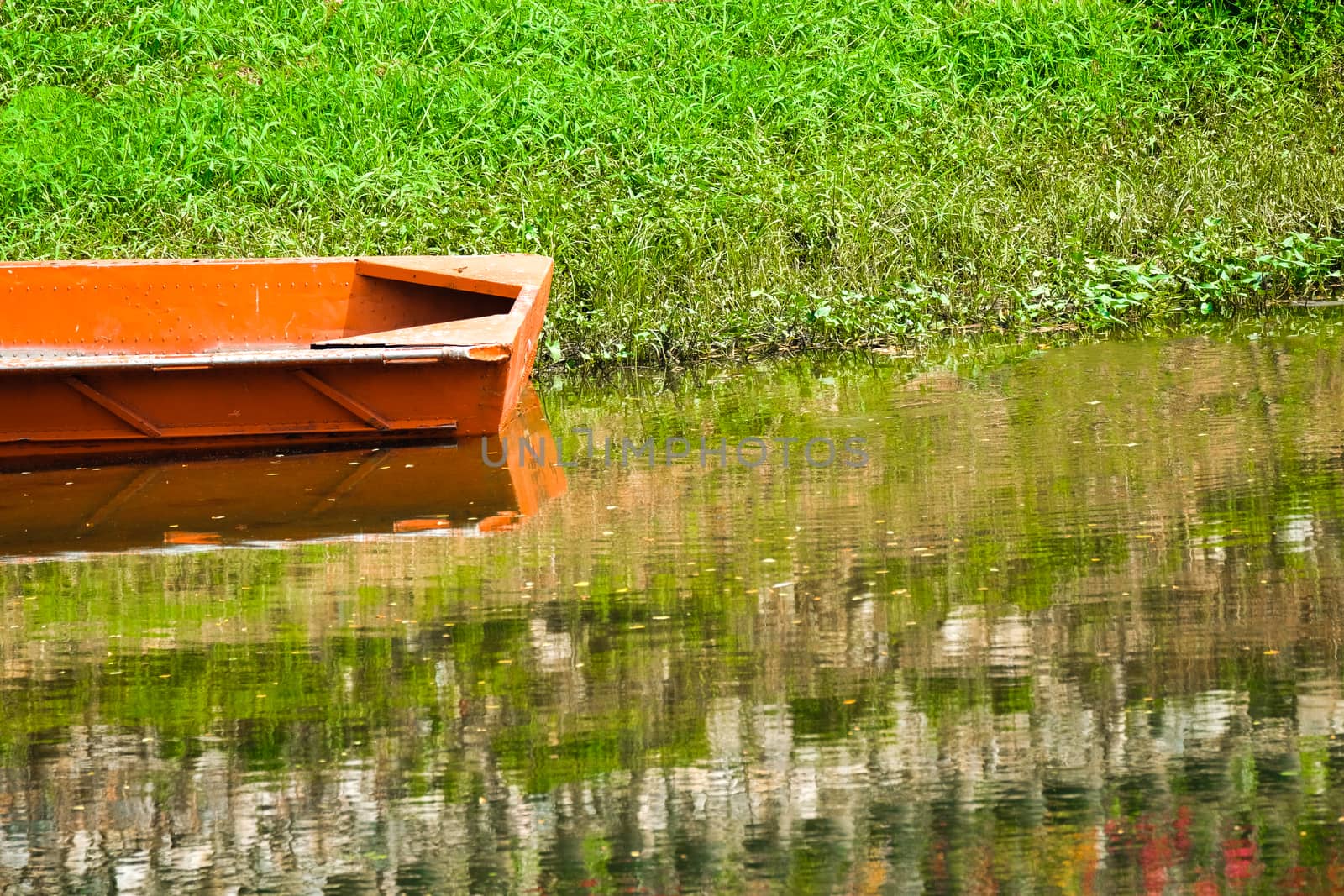 an abandonned rusty orange flat bottom boat resting by the bank of a shallow river