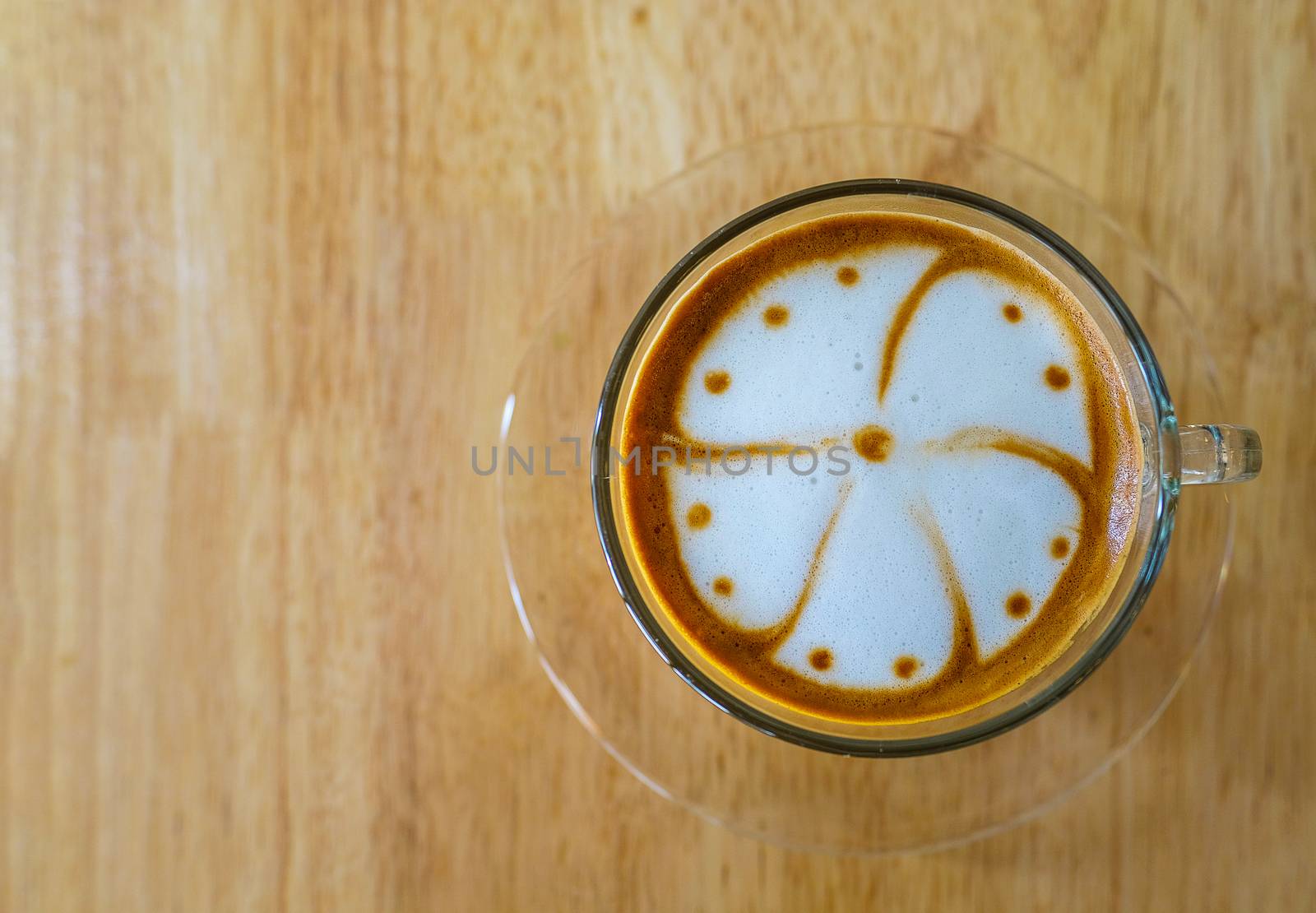 hot cappuccino coffee in a clear glass cup, on light brown table, top view, directly above