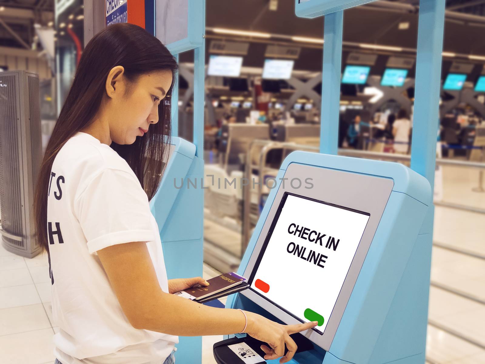 young Asian woman with passport using self check-in kiosk touch screen interactive display in airport, doing self check-in for flight or buying airplane tickets at automatic device in airport terminal by asiandelight