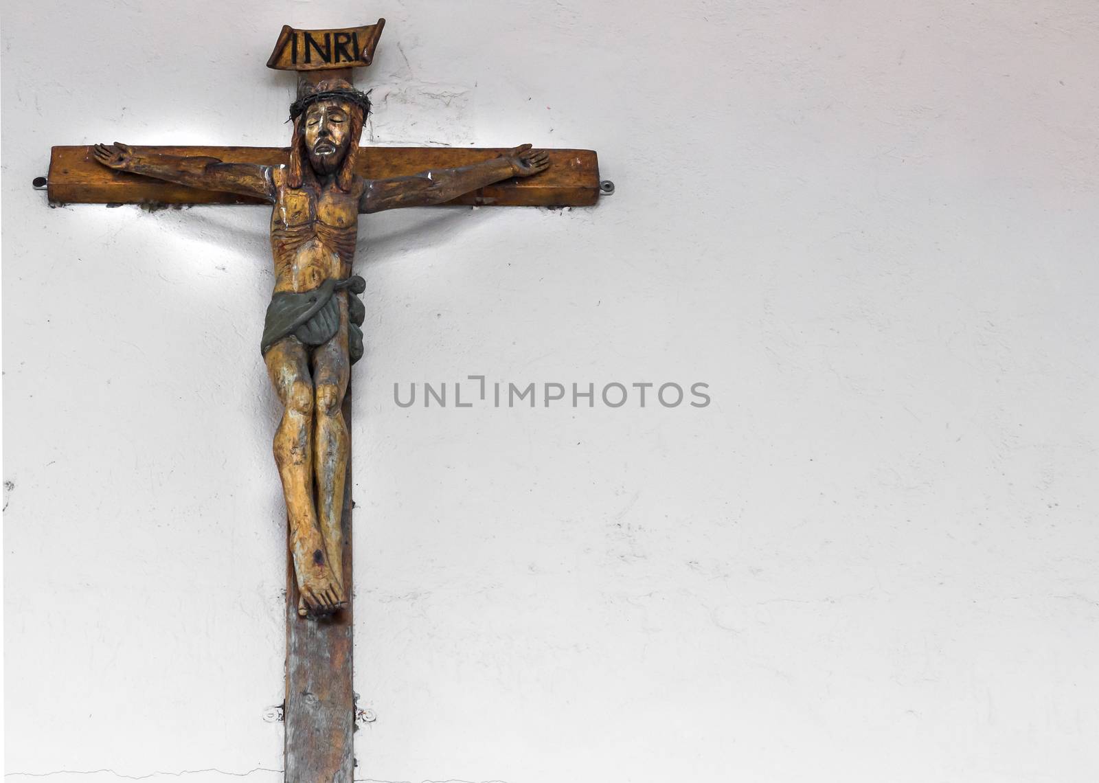 Small old wooden crucifix on a wall white as a background, with free space for text.