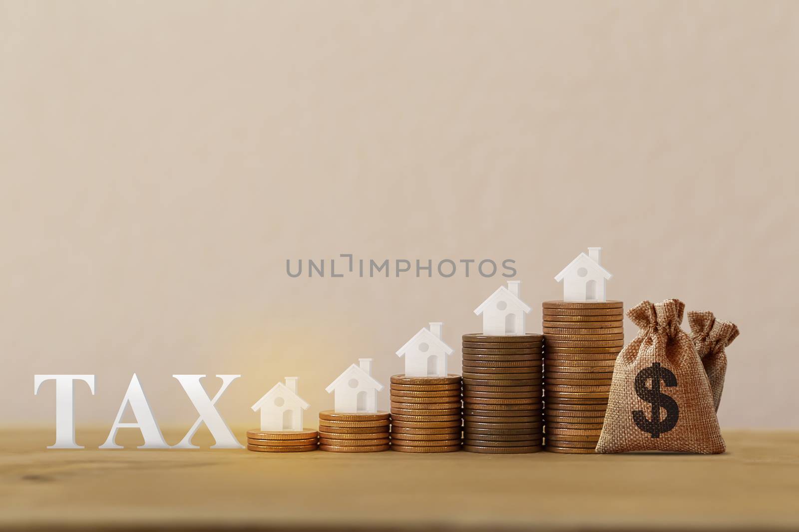Mini house on rows of rising coins, US dollar bags, word tax on wood table. House or housing, land value, finance tax concept: depicts ad valorem tax on the value of the property all.