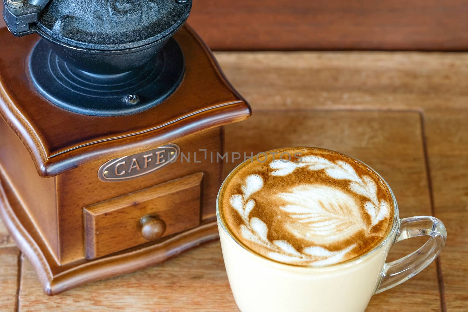 a cup of warm latte on a small wooden table with a vintage coffee grinder