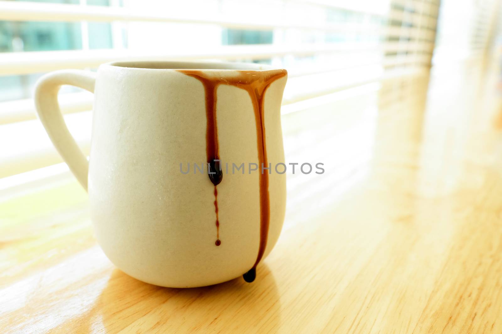 few drops of chocolate syrup on the side of a ceramic mug on top of a wooden counter by a glass window