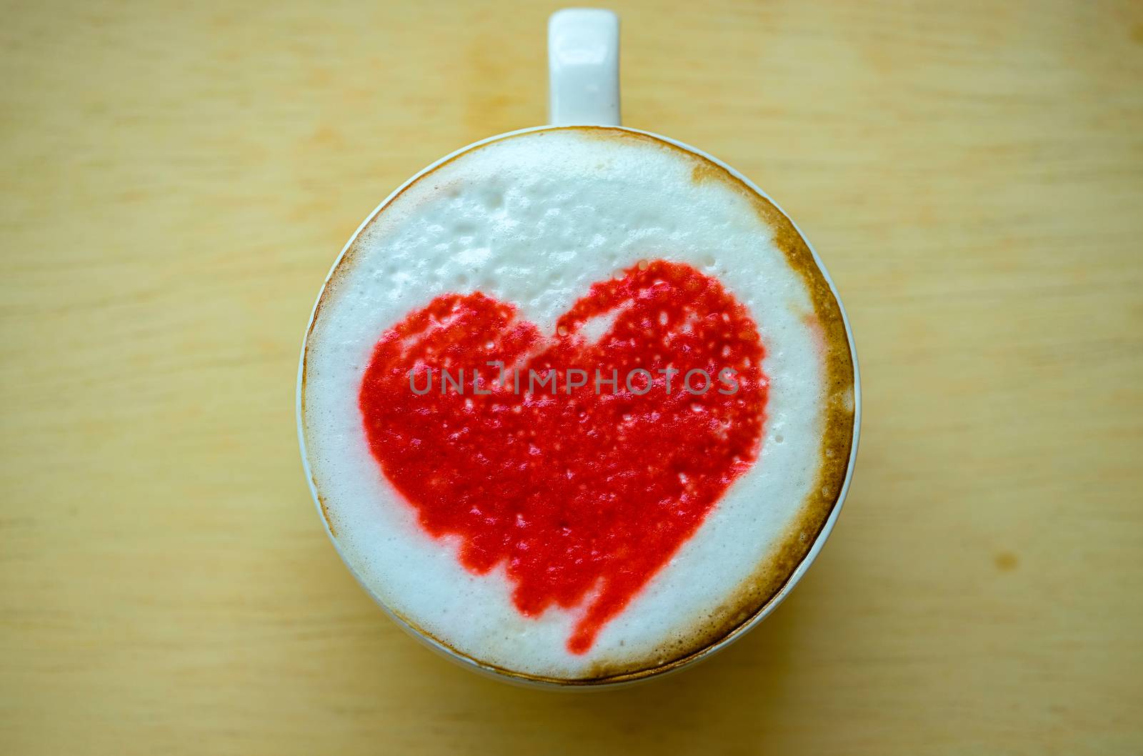 hot coffee in a white ceramic cup with red latte art, wooden background