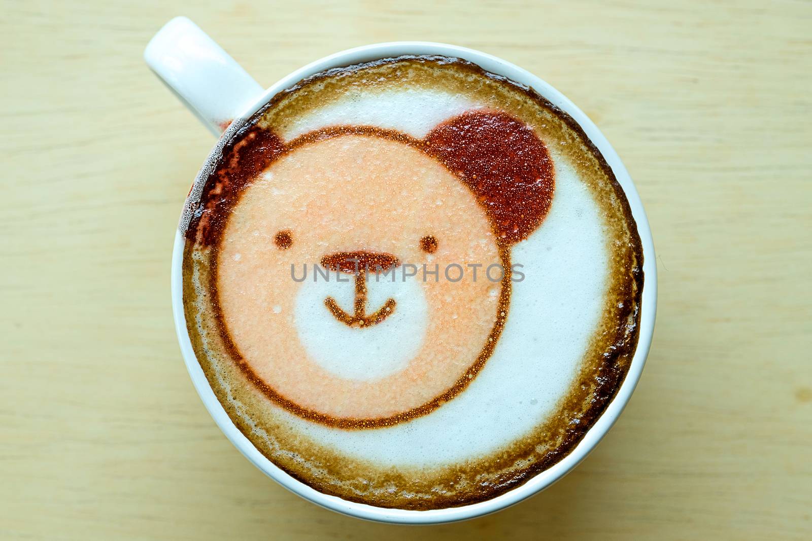 hot coffee in a white ceramic cup with cute bear face latte art, wooden background