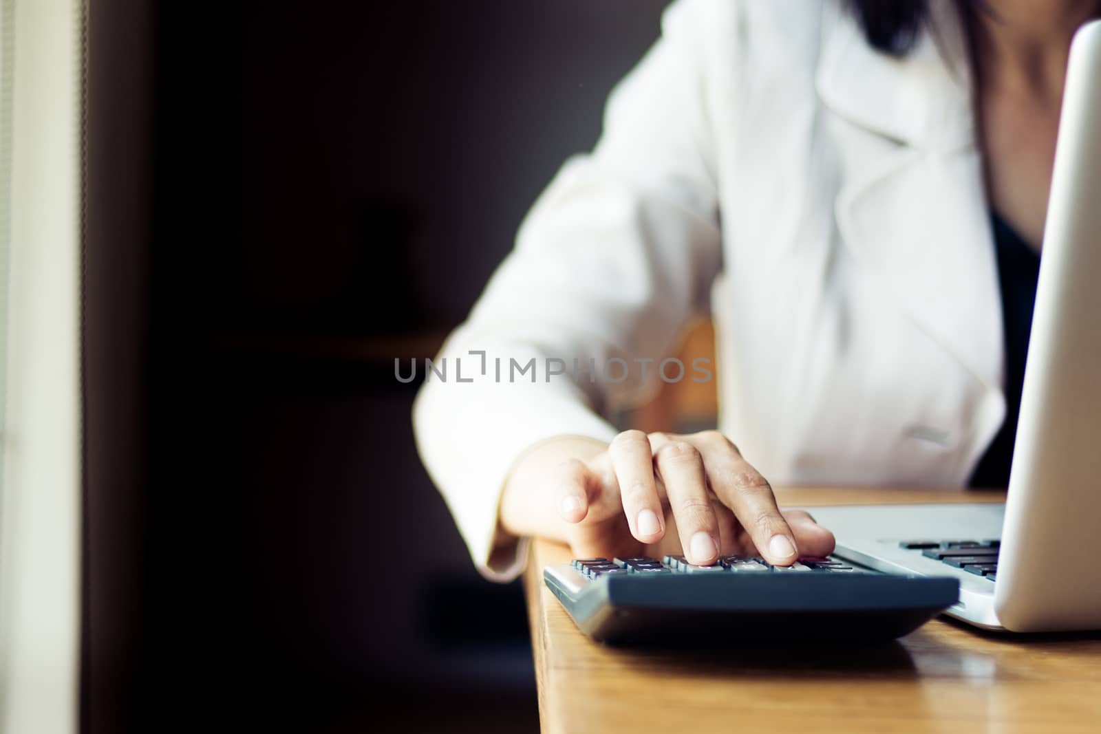 Asian business woman using calculator for accounting and analyzing investment in front of computer laptop at office workspace.  banking , savings , accountant , finances and economy concept.