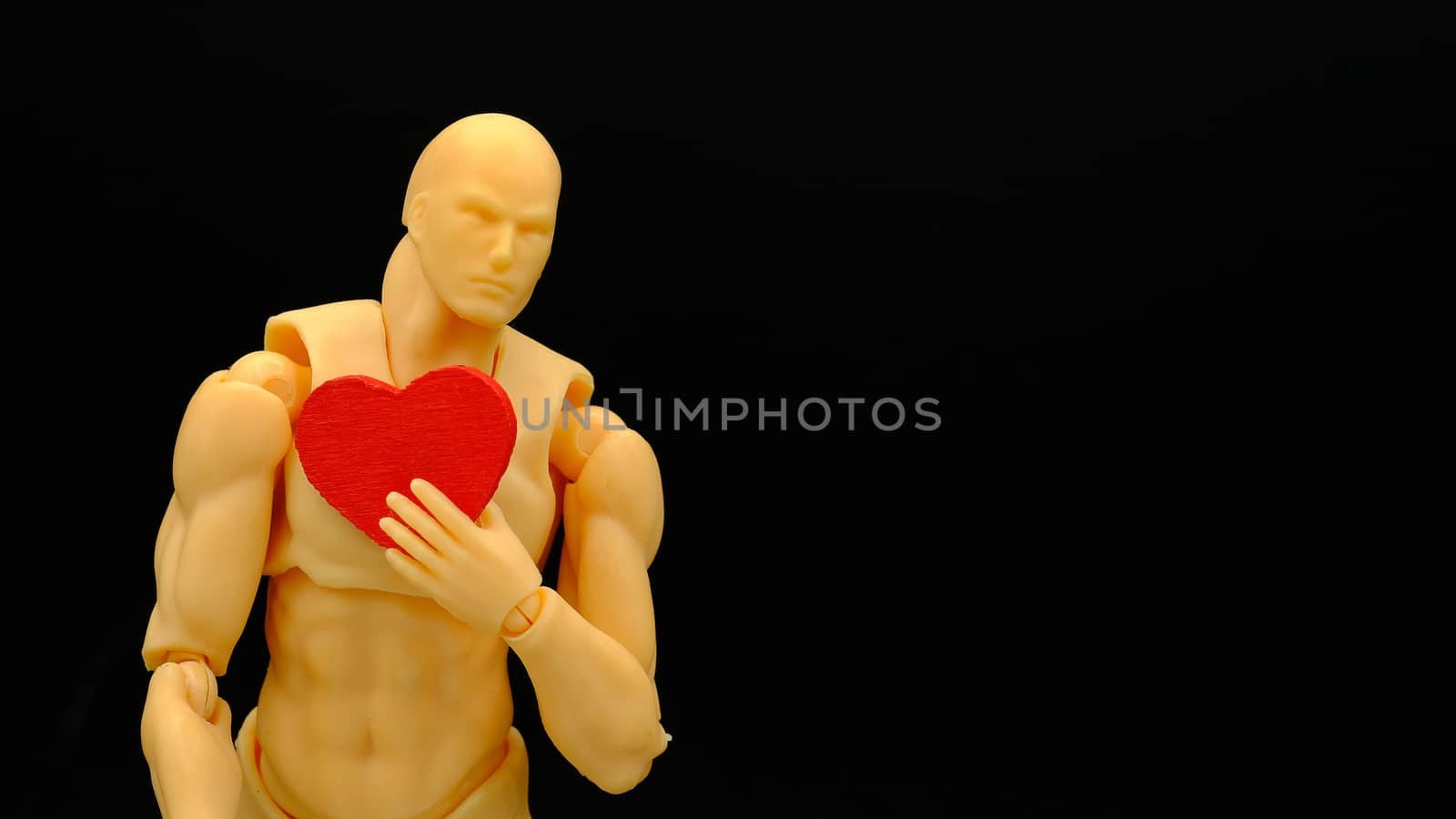 a human model holding a piece of wooden red heart , isolated on black background