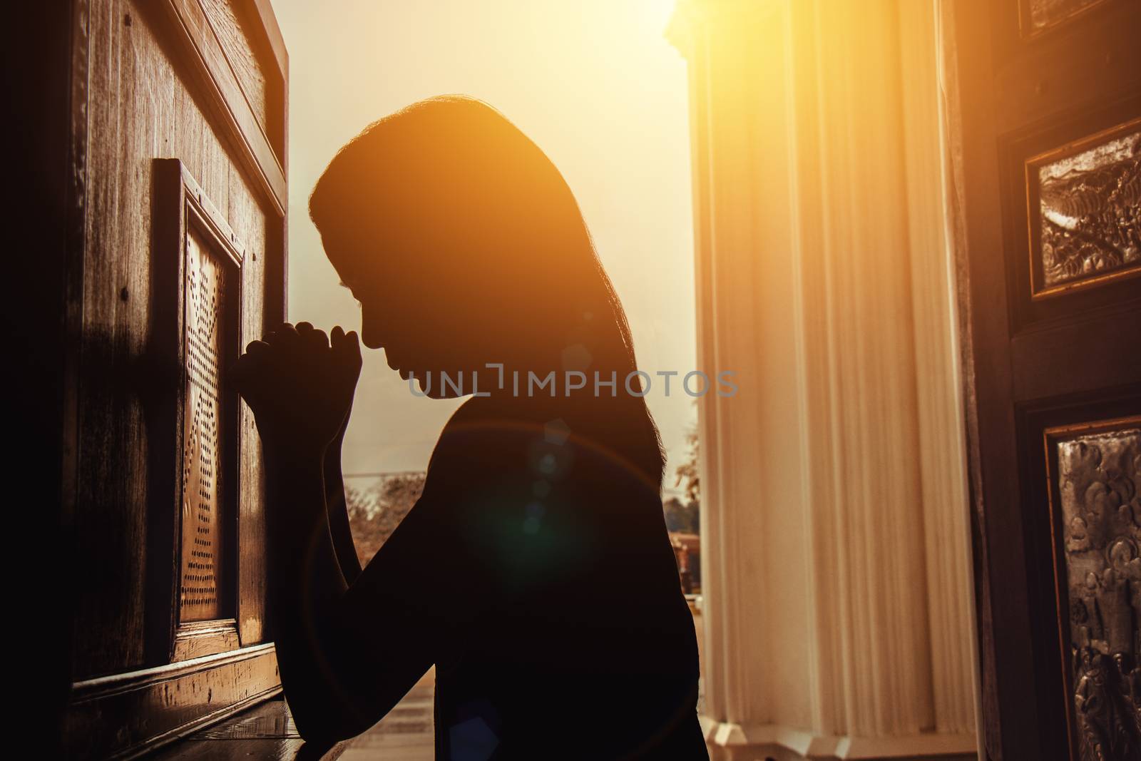 silhouette of woman kneeling and praying in modern church at sunset time by asiandelight