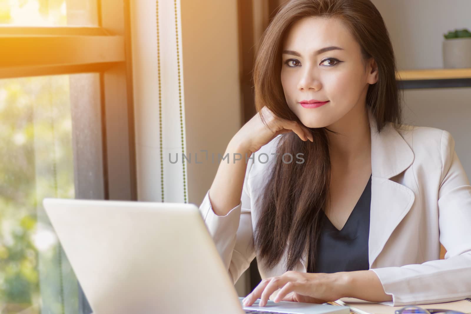 startup business in Asia concept. focused young Asian business woman with thinking face working with laptop at workplace looking at camera, film effect and sun flare effect.