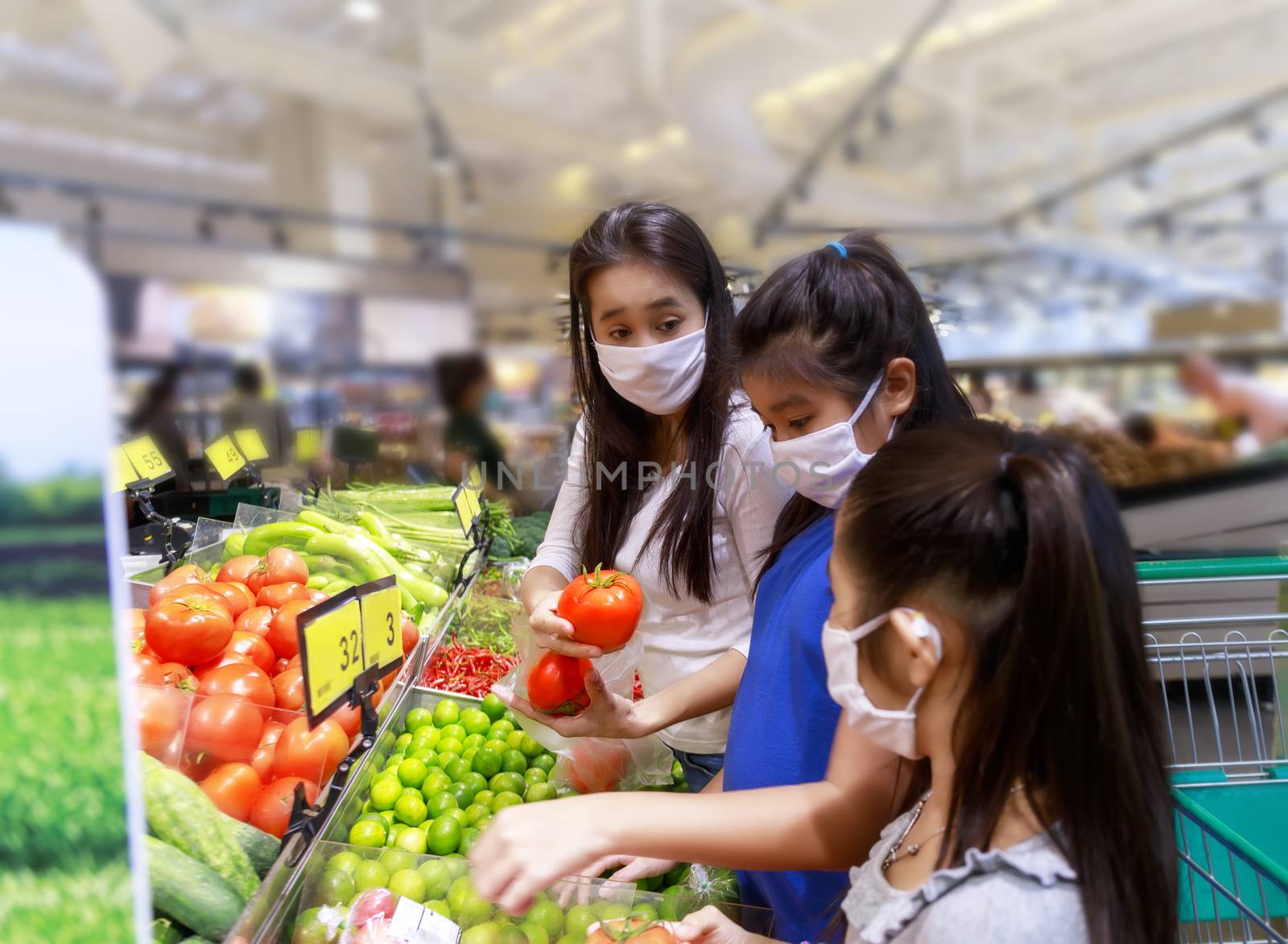 Asian woman with her daughter wear protective face mask in supermarket departmentstore. Mom ฟืก daughter looking grocery to buy  ดruit and vegetable. Womenhold red tomatos. Soft focus and selective Women. New normal after covid-19. Family concept.
