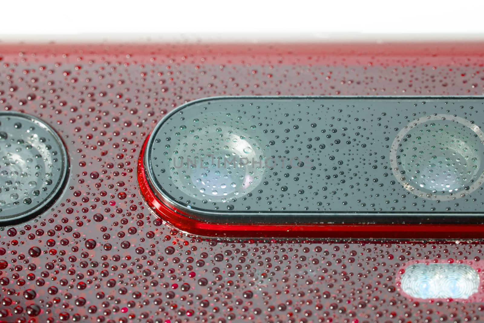 red phone camera lens covered with small water drops - close-up with selective focus and blur.