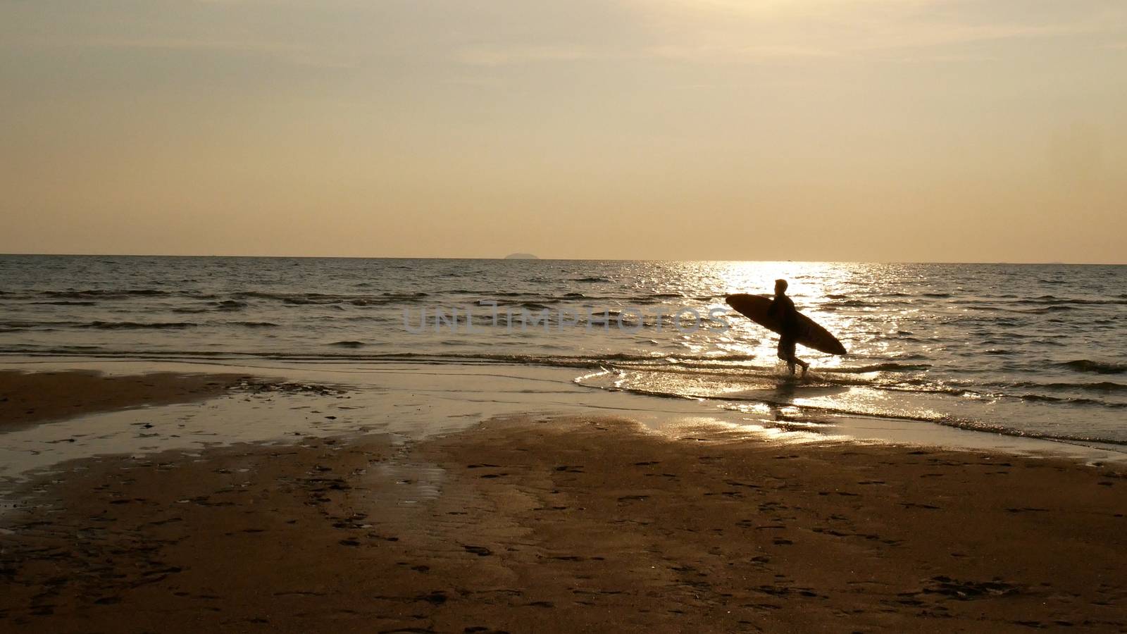 Silhouette of surf man with surfboard running on water surface. Surfing at sunset beach. Outdoor water sport adventure lifestyle.Summer activity. Handsome Asia male model in his 20s. by asiandelight