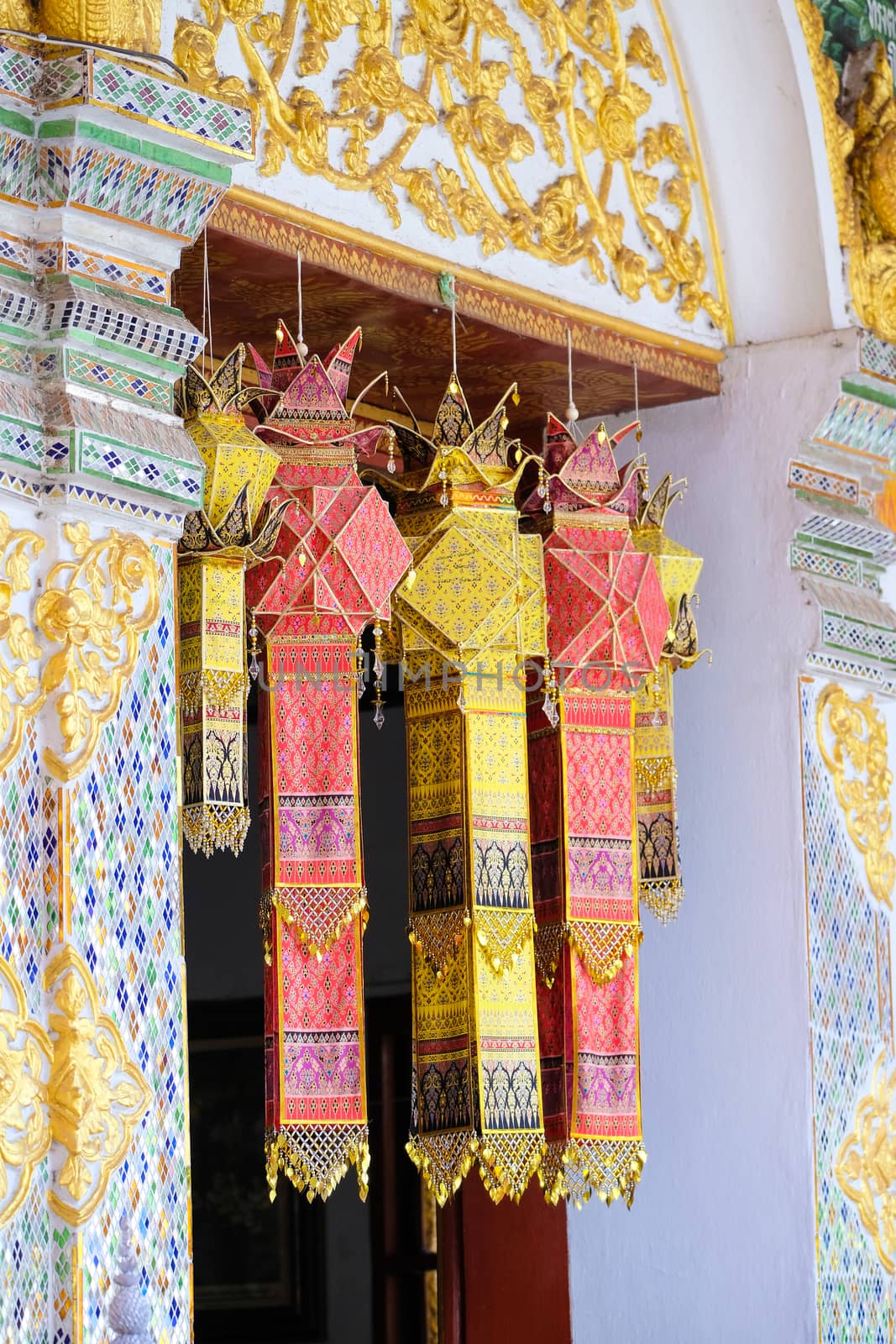 a group of colorful traditional hand painted silk cloth lanterns decorating the window of the main temple of Wat Phra That Hariphunchai, the iconic Buddhist landmark in Lamphun City, Thailand