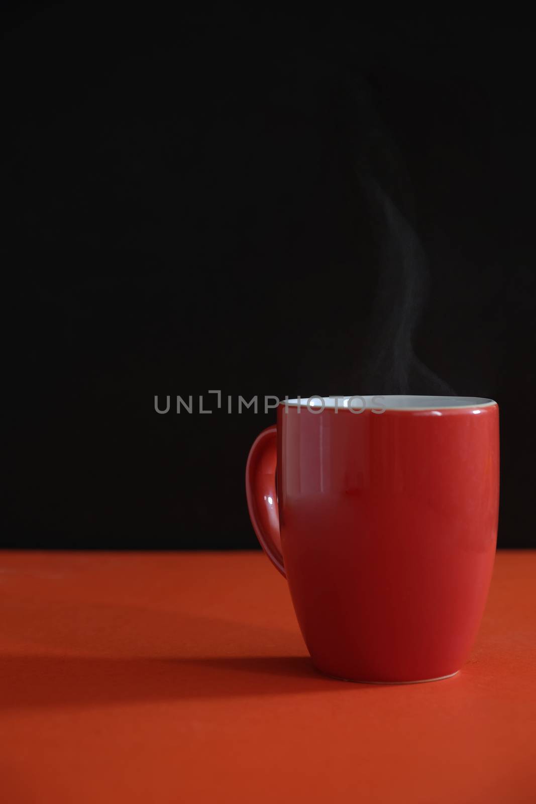 an orange mug with steamy hot coffee on an orange table top with dark background