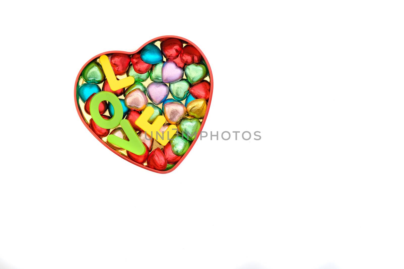 heart-shaped chocolate candies in various colors in a heart-shape tin box together with letters spelling LOVE, Valentines' Day, romantic concept, top view, isolated on white, with copy space