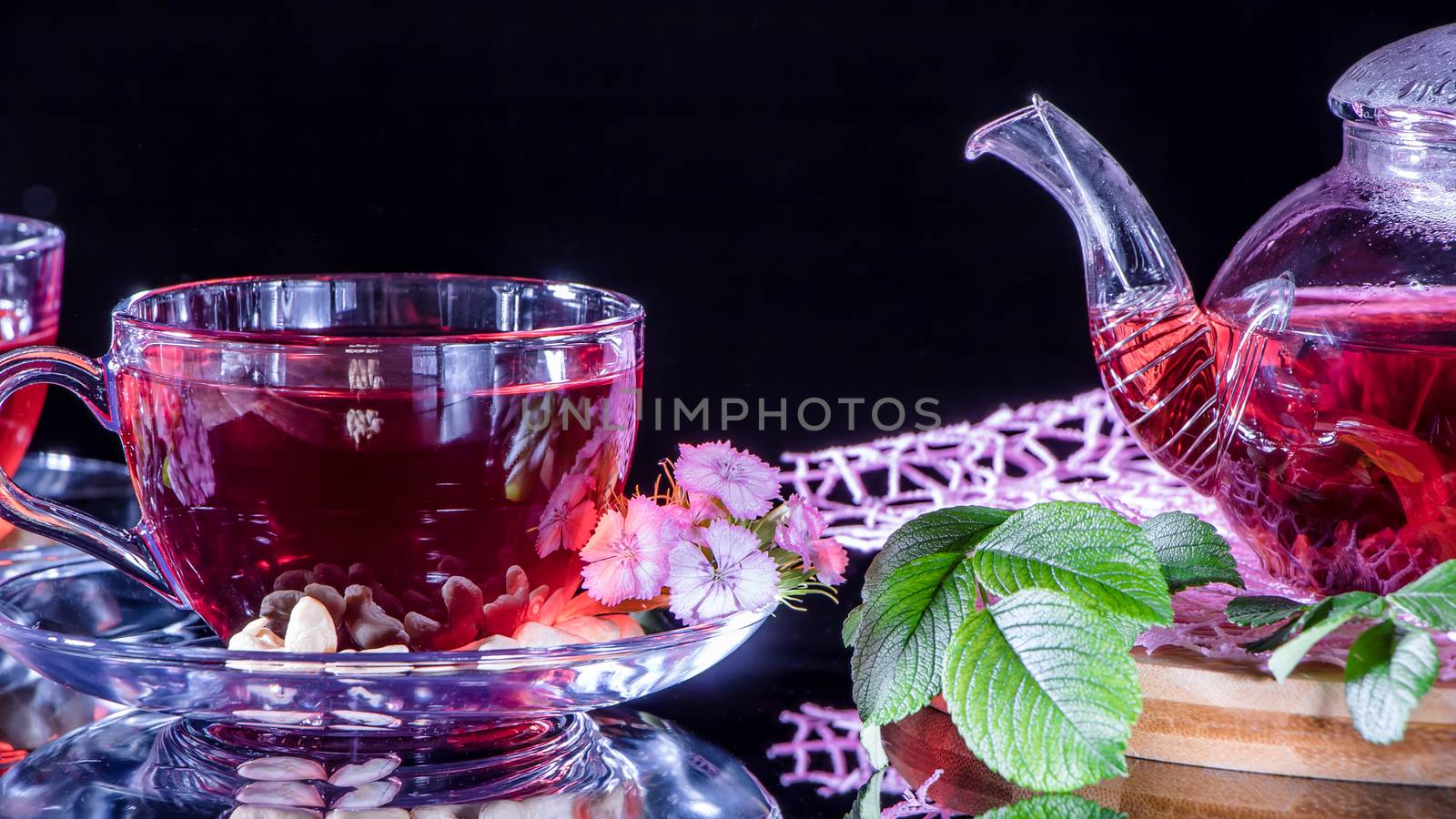 A mug of red tea and a teapot in white hibiscus flowers and green leaves of medicinal tea on a wooden stand.Zen tea ceremony. Photo of red herbal Indian healing tea.Elegant mugs with a relaxing drink