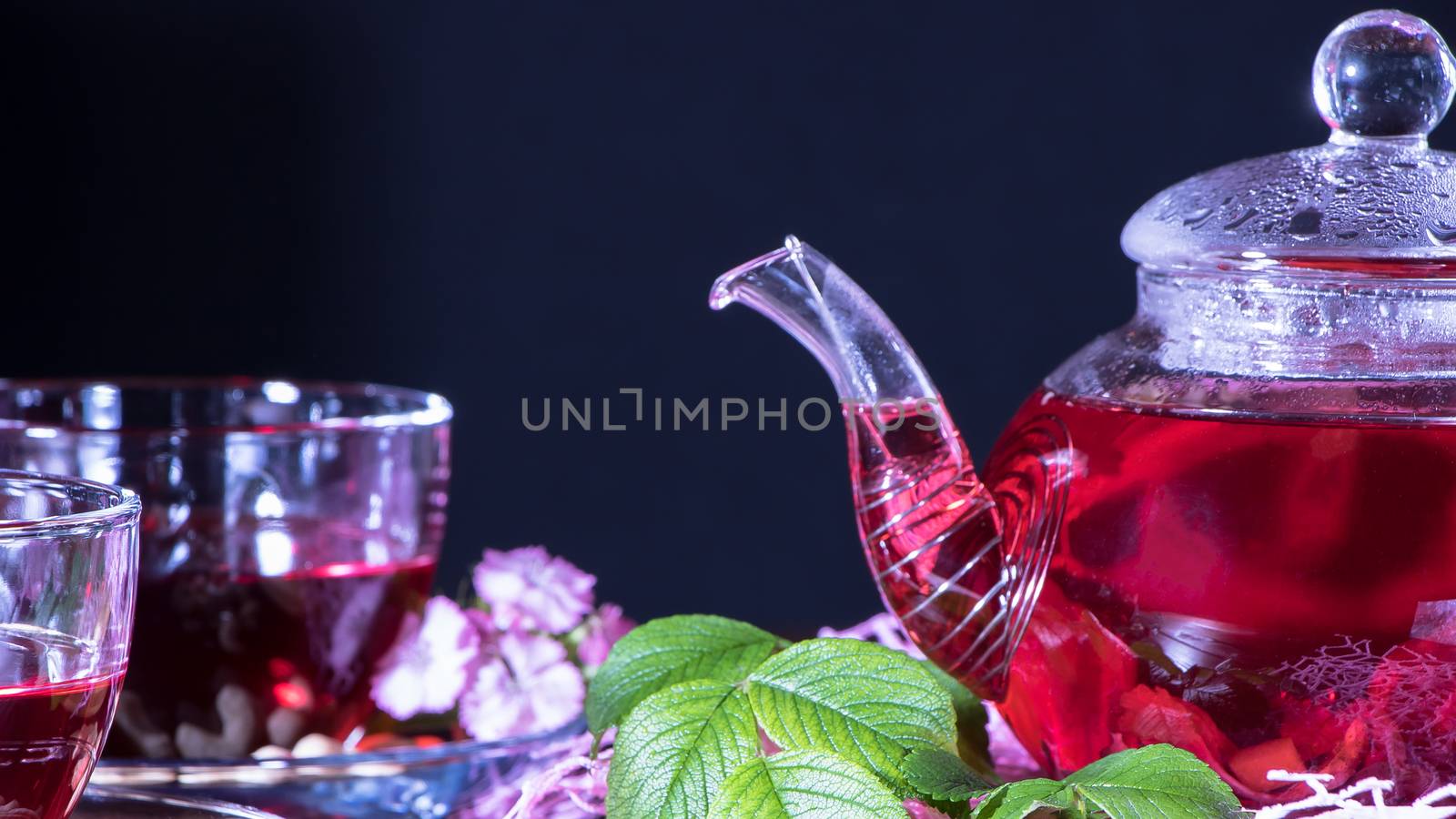 A mug of red tea and a teapot in white hibiscus flowers and green leaves of medicinal tea on a wooden stand.Zen tea ceremony. Photo of red herbal Indian healing tea.Elegant mugs with a relaxing drink