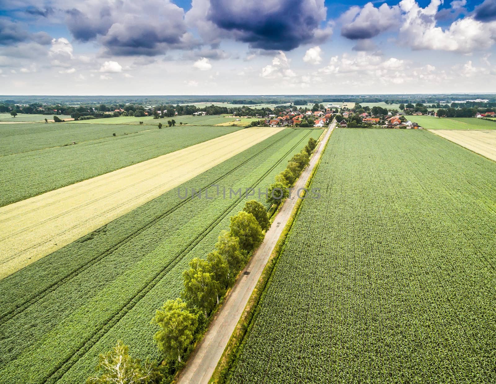 The road to the village through fields and meadows, abstract aerial photo with dramatic clouds, high location with the drone.