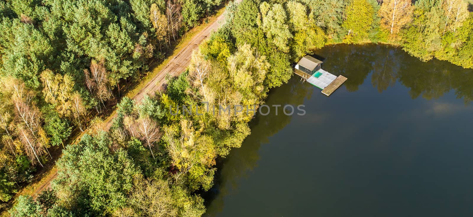 Fishing lodge in the corner of a pond, path with trees, aerial view with drone