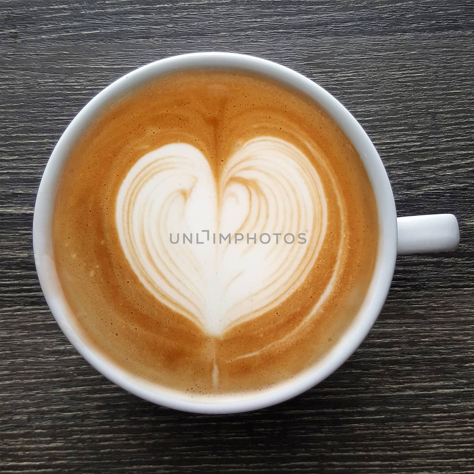 Top view of a mug of latte art coffee on timber background.