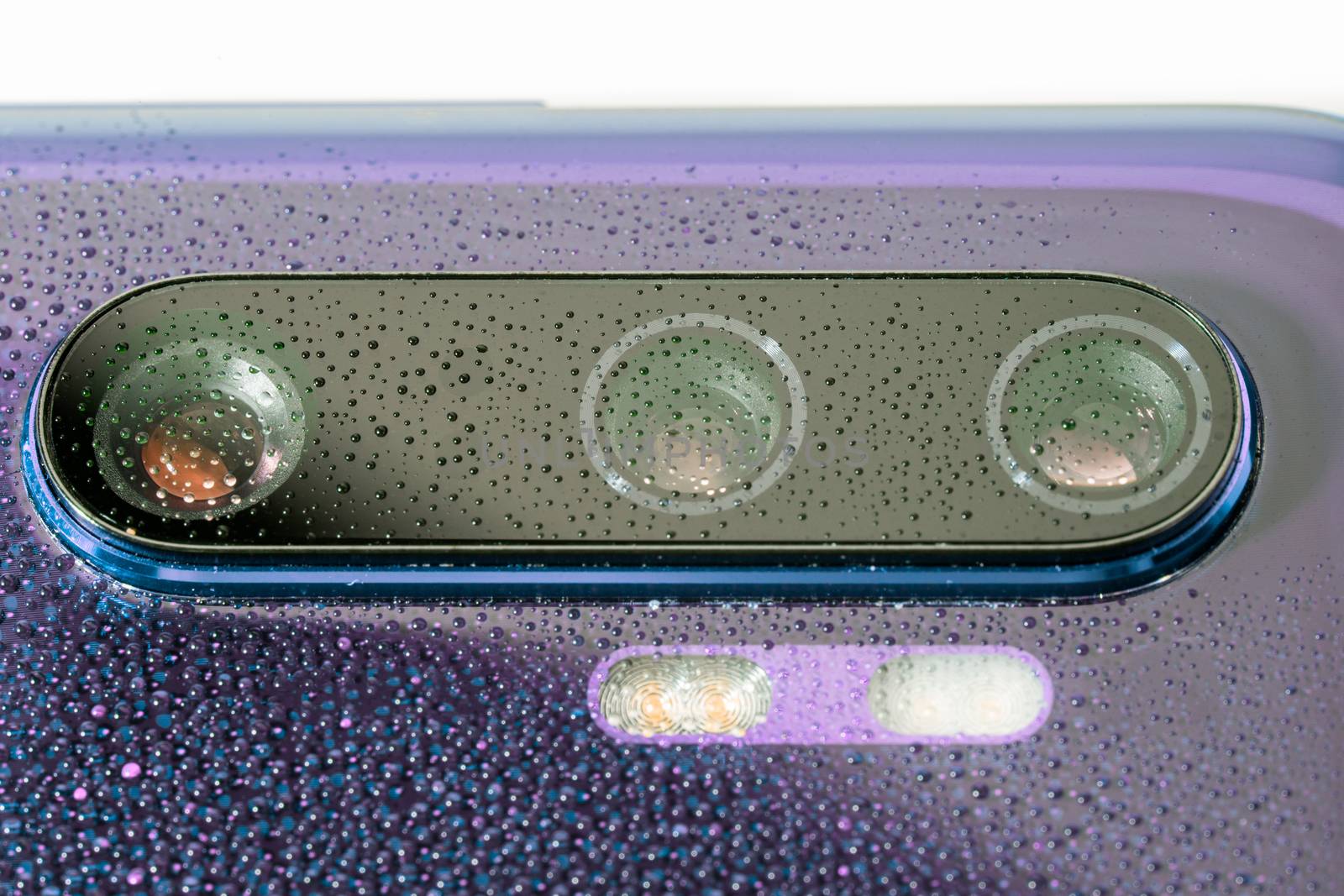 purple phone camera lens covered with small water drops - close-up with selective focus and blur.