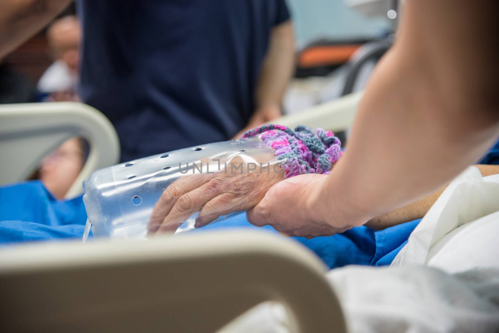 Patient in the hospital with saline intravenous and relatives patient hand holding a elderly patient hand with DIY restraint gloves