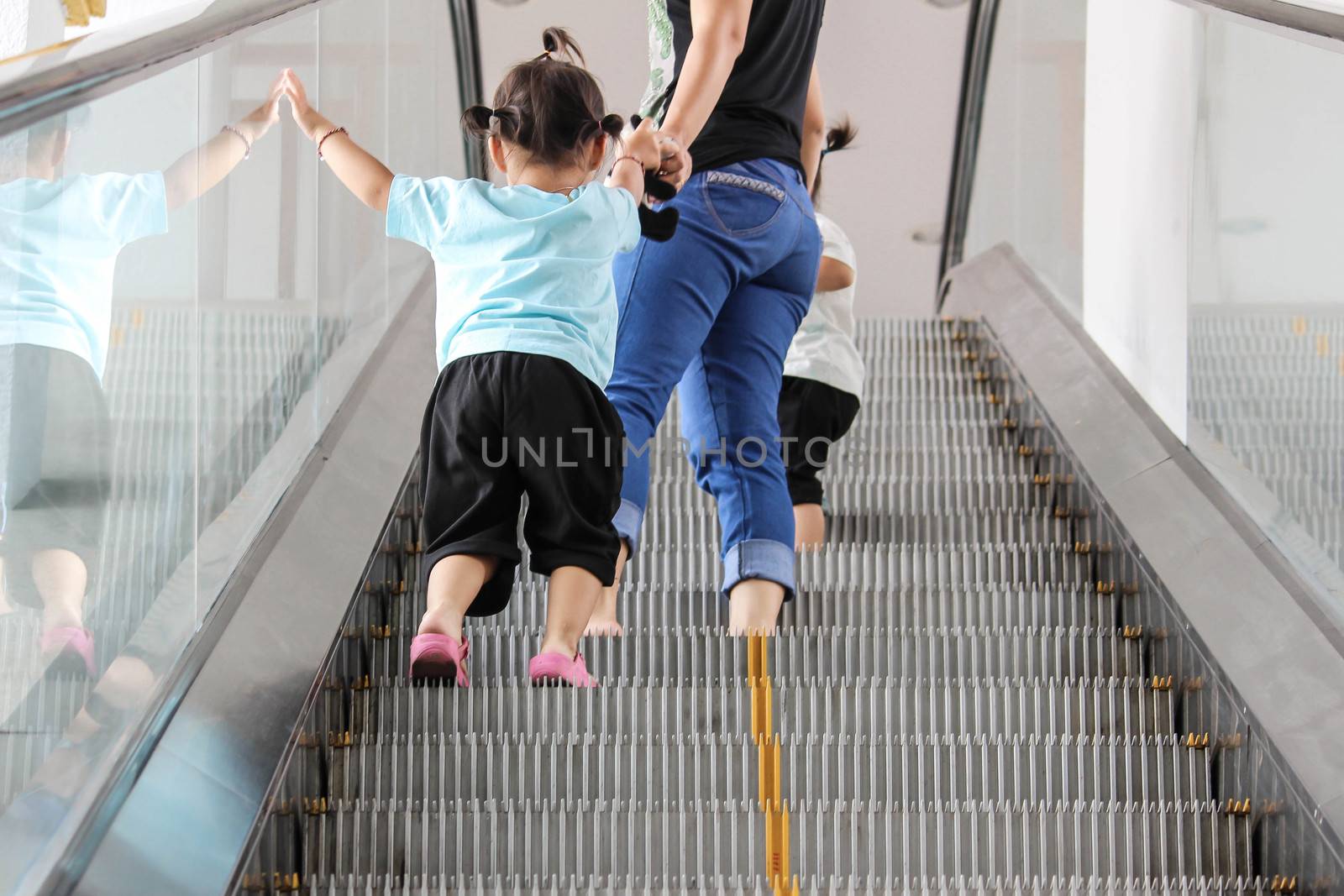 Back view of mother and child walking up together on broken escalator background.