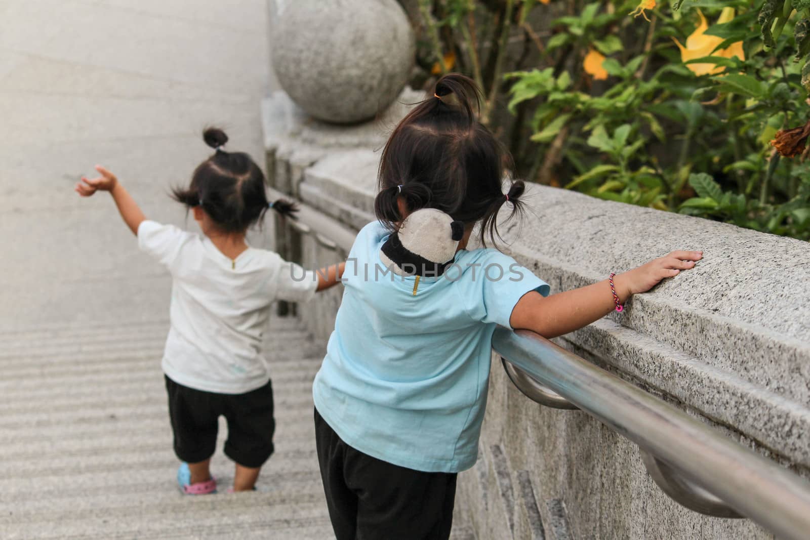 Asian little girl with sister walking down the stairs outdoors by themself. View from the back. Dangerous in children. by TEERASAK